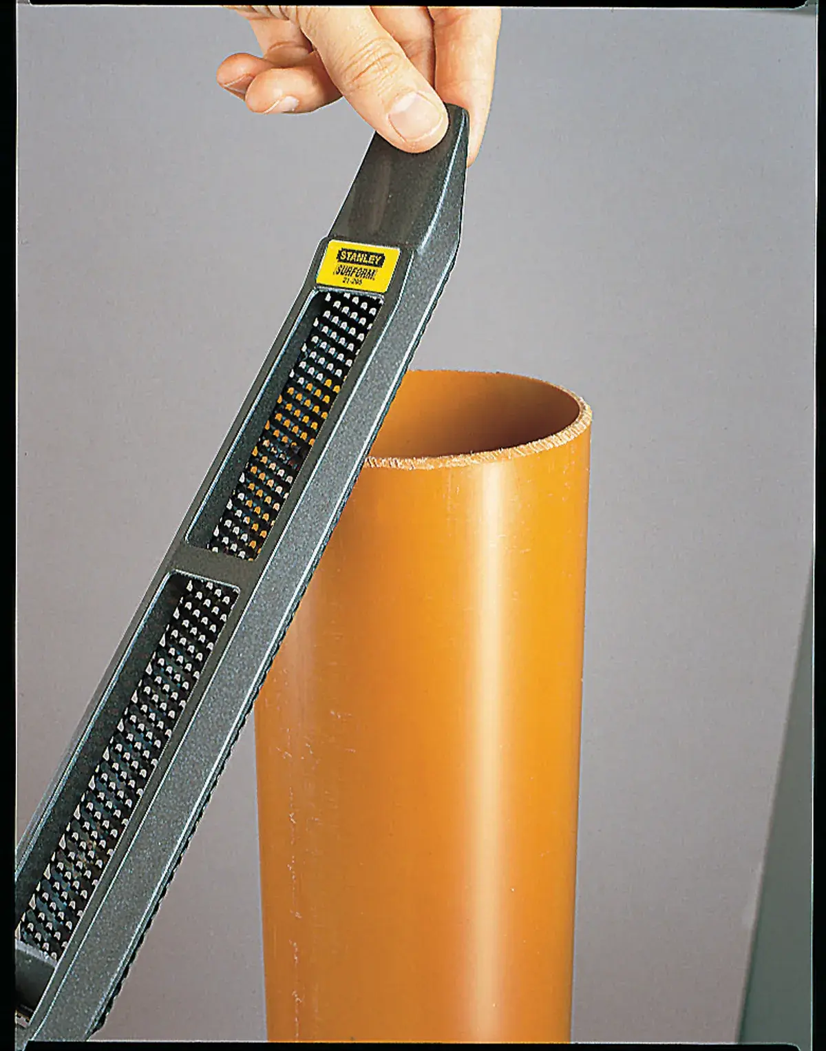 Foto de la escofina manual STANLEY 21-295 alisando el borde de un tubo plástico naranja.