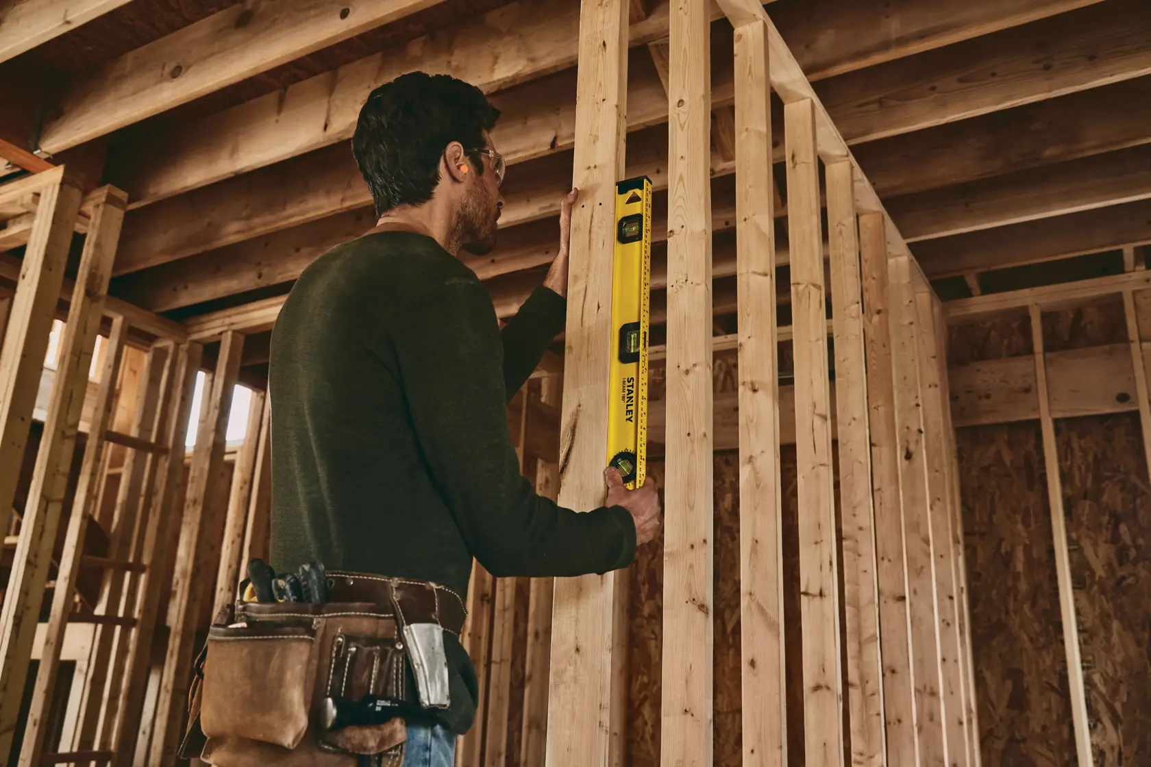 Herramienta de nivel STANLEY 42-324 usada por trabajador verificando la alineación vertical de vigas de madera en obra.