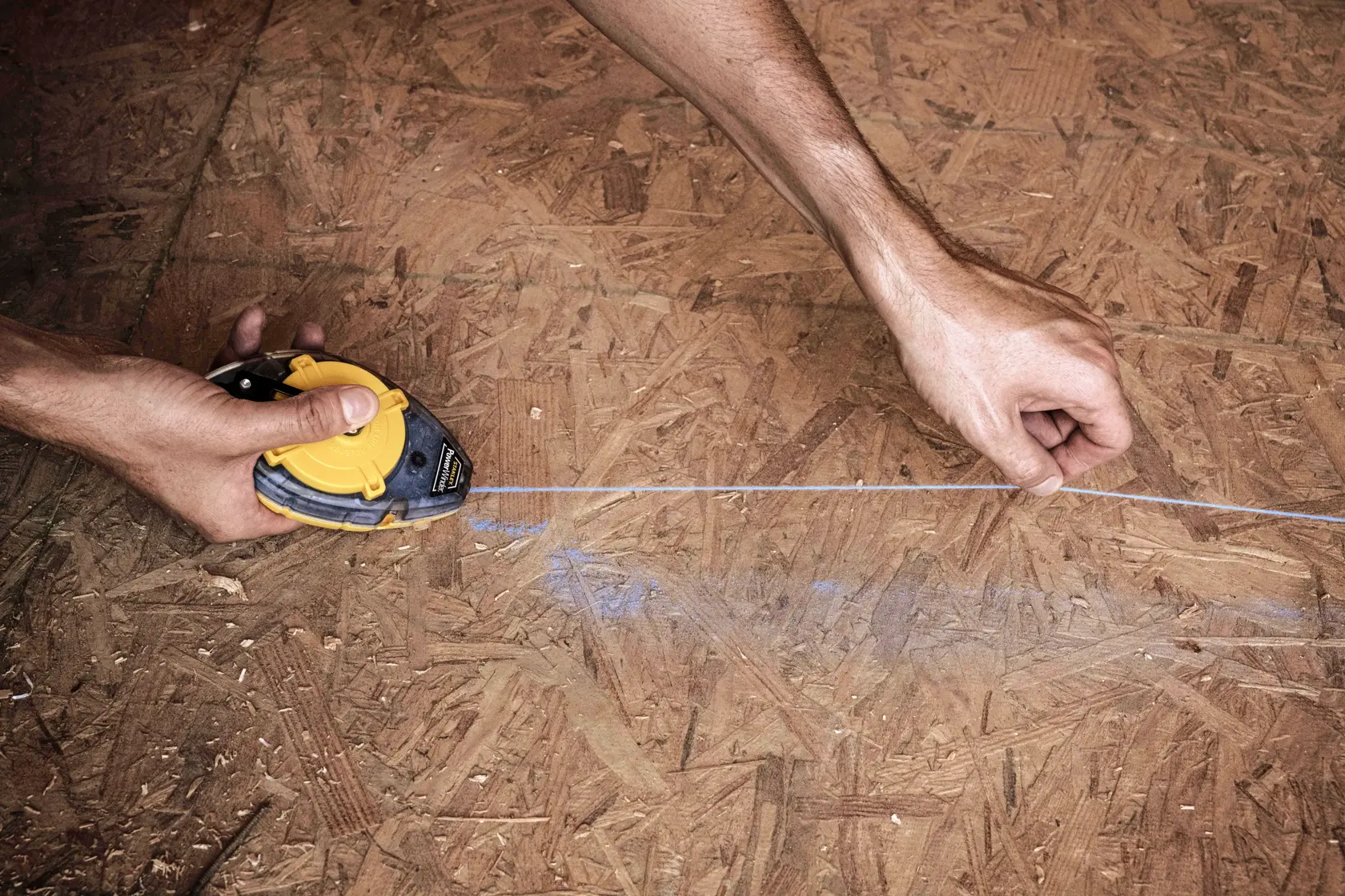 Fotografía de herramienta de línea de tiza STANLEY 47-464 marcando superficie de madera contrachapada, primer plano.