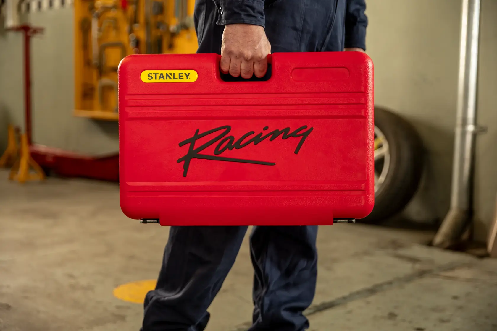 Maleta de ferramentas vermelha STANLEY R99-120LA com logo Racing preto, carregada por pessoa em oficina.