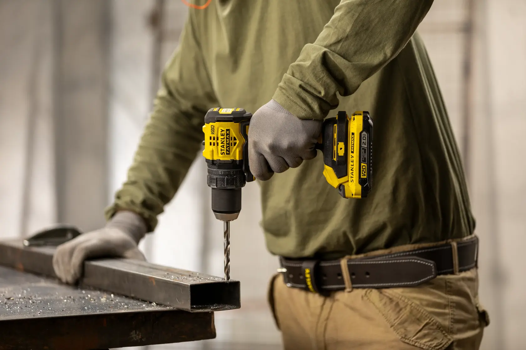 Taladro inalámbrico STANLEY SBD714 usado para perforar una viga metálica, operado por trabajador con guantes.