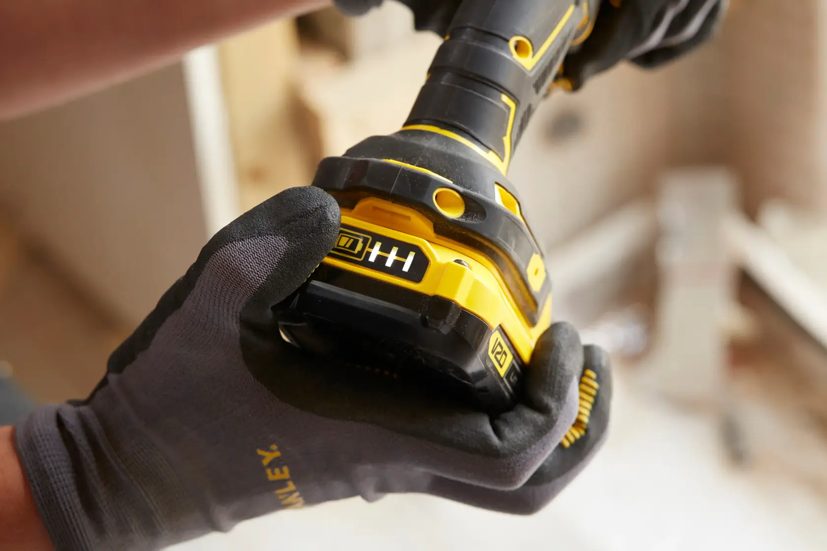 Foto en primer plano de un taladro inalámbrico STANLEY SCD700C2K-B3 sostenido con guantes mostrando el indicador de batería.