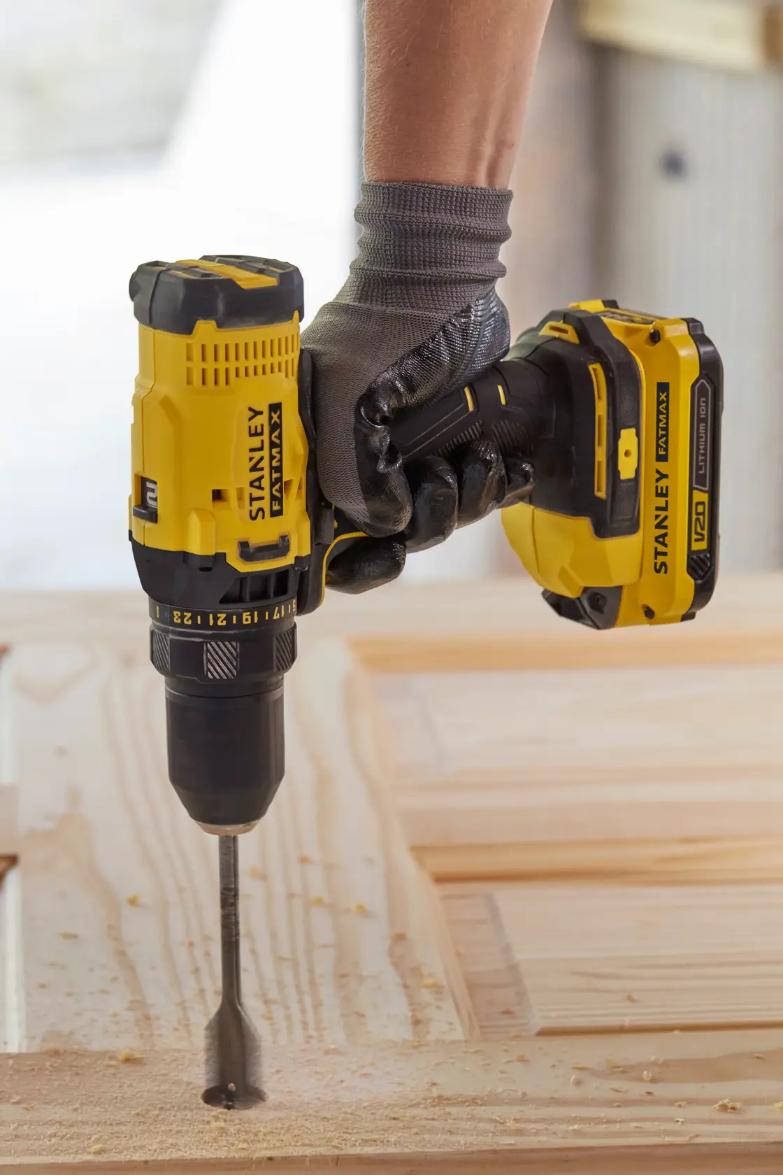 Fotografía del taladro inalámbrico STANLEY SCD700C2K-B3 en uso, perforando madera, primer plano de la herramienta y mano con guante.