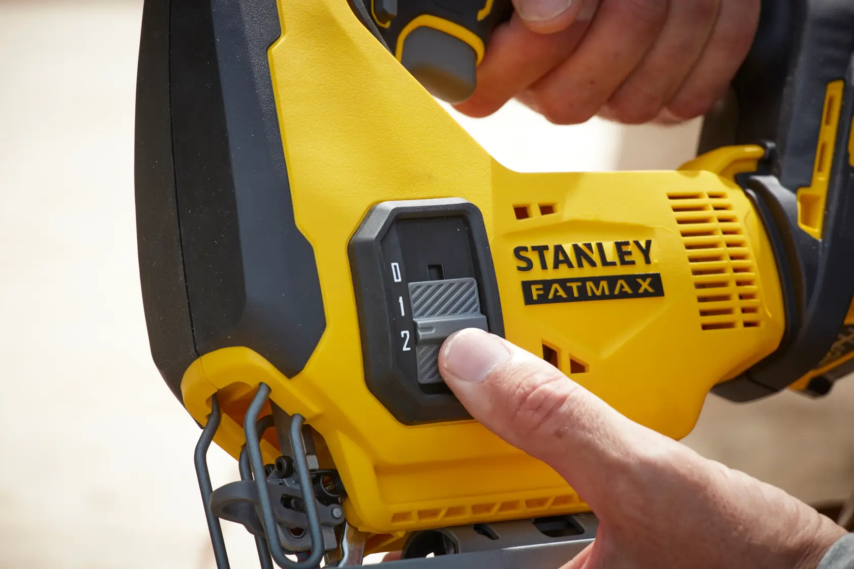 Foto en primer plano del interruptor de ajuste de la sierra caladora STANLEY FATMAX SCJ600M2K con mano controlando la velocidad.