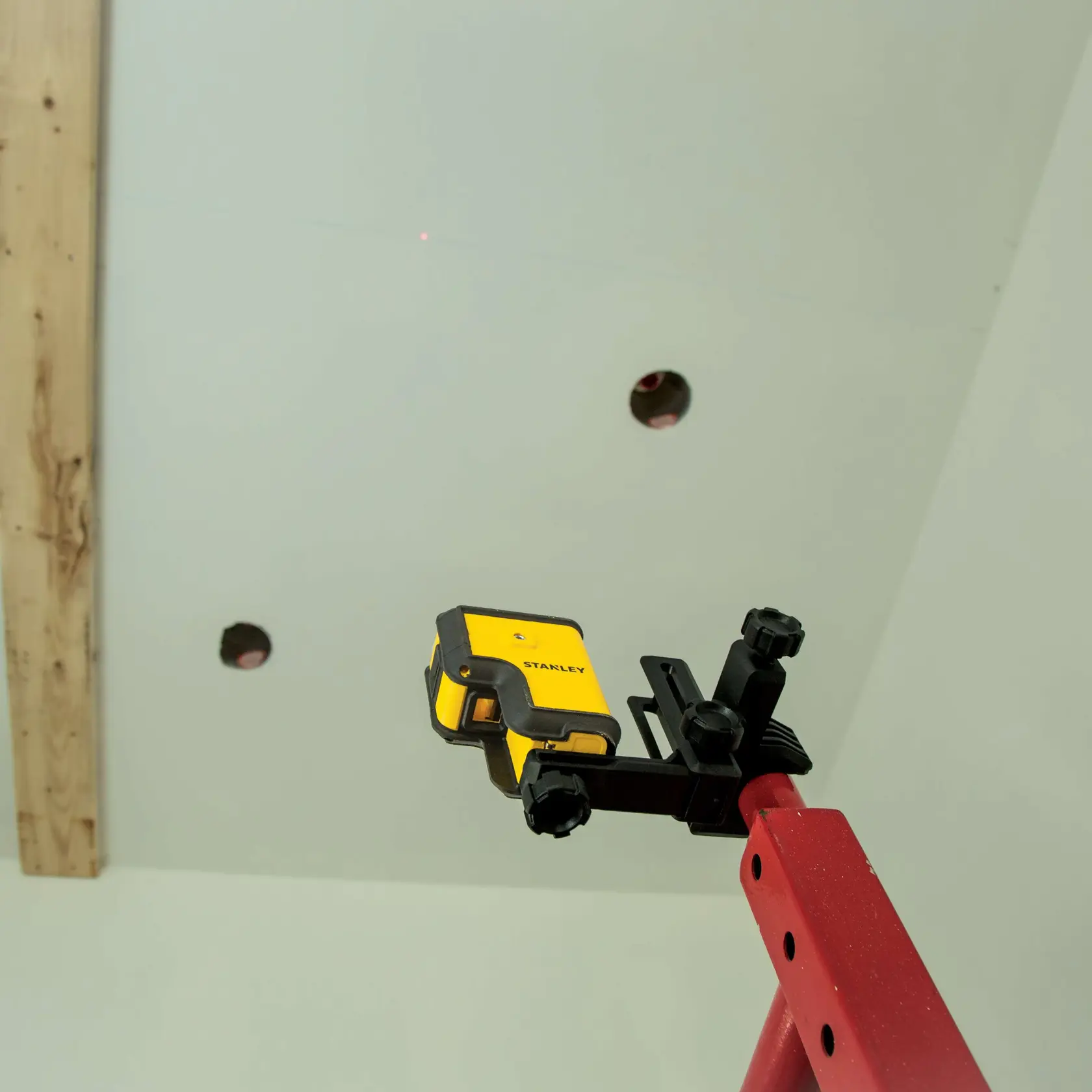 Fotografía de nivel láser STANLEY STHT77503 montado en poste rojo, apuntando al techo con agujeros.