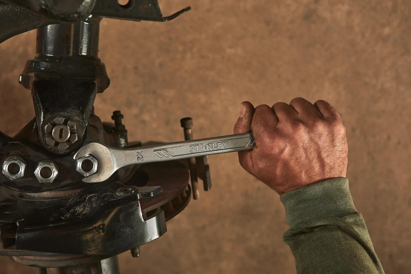 Llave STANLEY STMT72819 usada por una mano para apretar un perno en equipo mecánico, primer plano en taller.