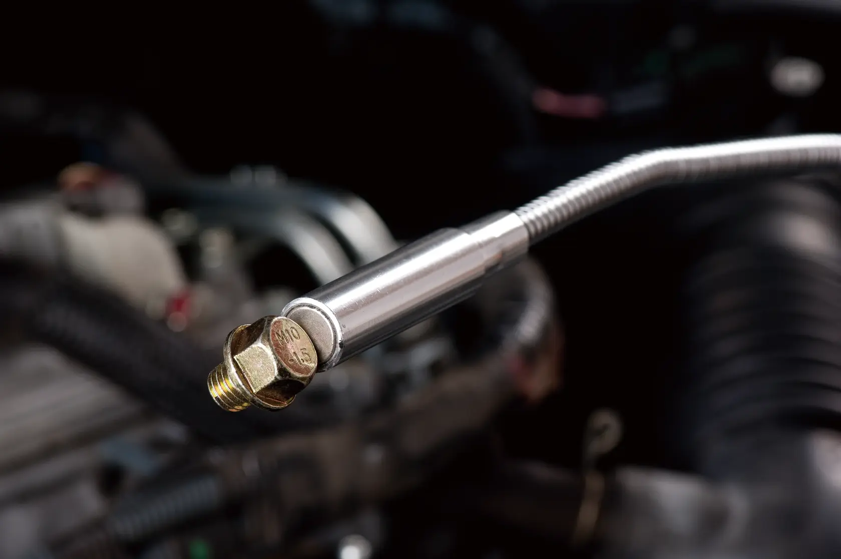 Herramienta magnética flexible STANLEY STMT78241-8 sosteniendo un perno de latón en contexto automotriz.