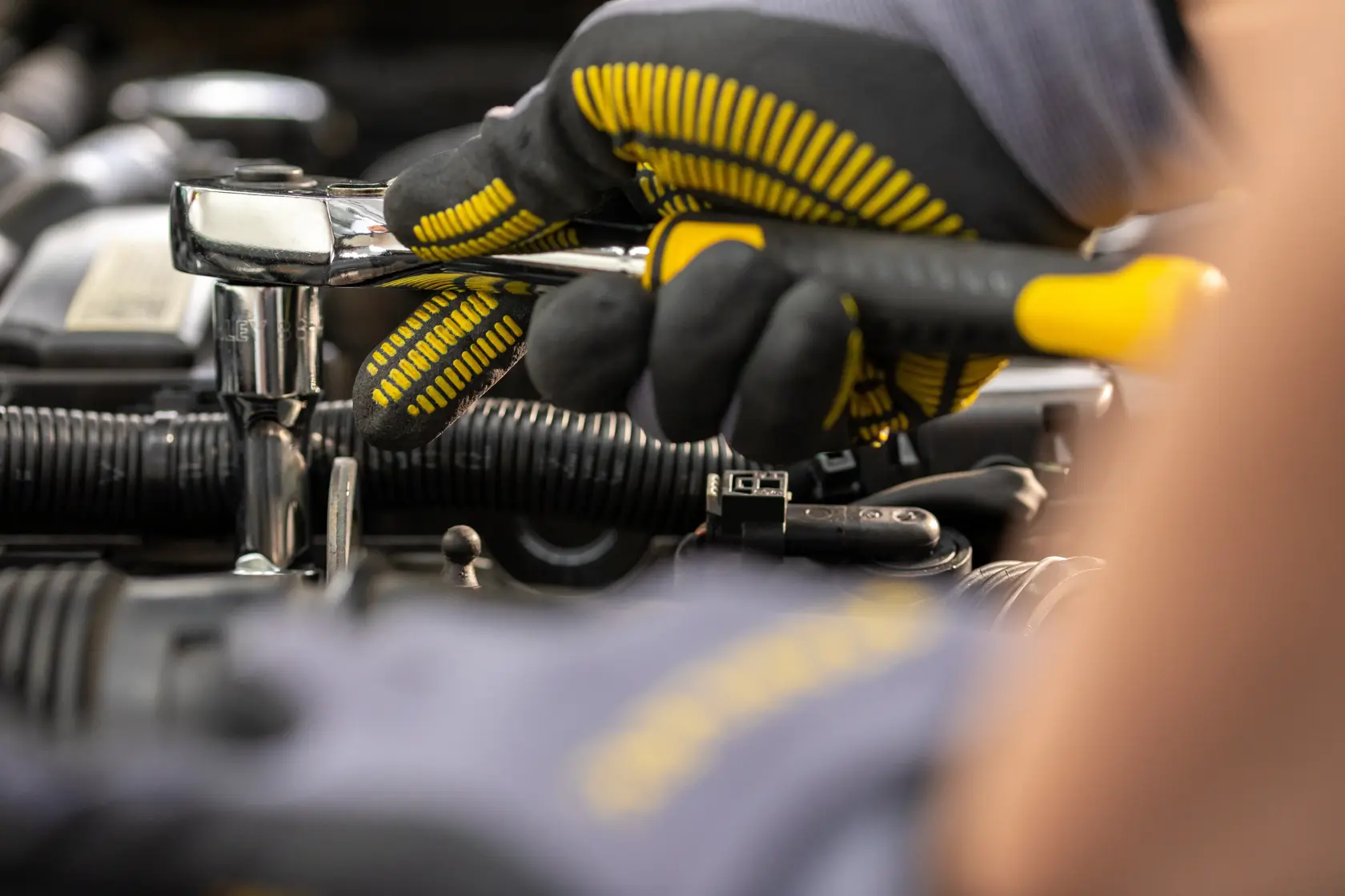 STANLEY STMT82665-0 llave de carraca usada por mano enguantada en motor automotriz, fotografía en primer plano.