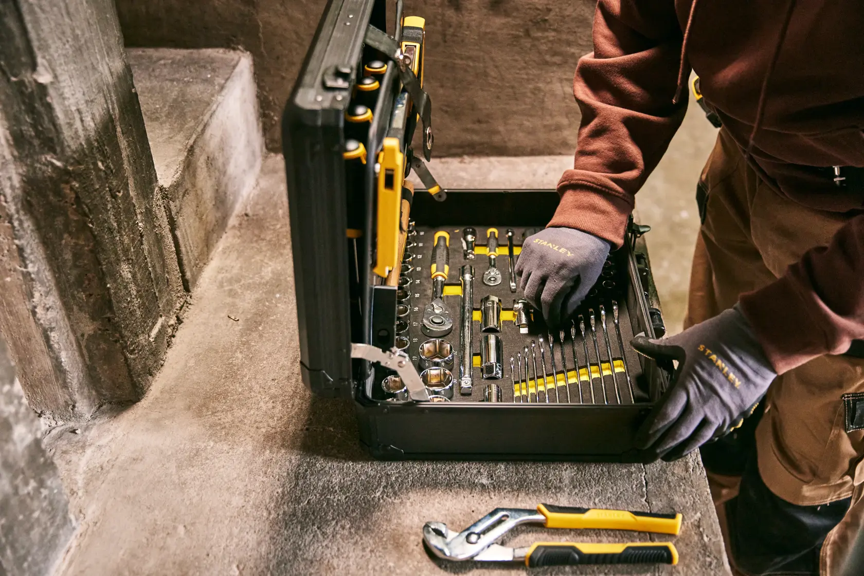 STANLEY STMT98109-LA conjunto de ferramentas em estojo preto, ferramentas variadas, trabalhador utilizando, fotografia em superfície de concreto.