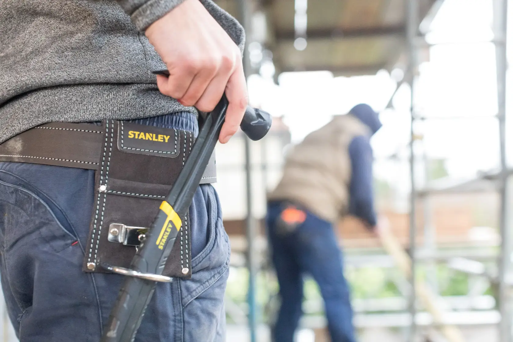 Martelo STANLEY STST1-80117 com cabo amarelo e preto segurado por trabalhador com luvas em canteiro de obras.