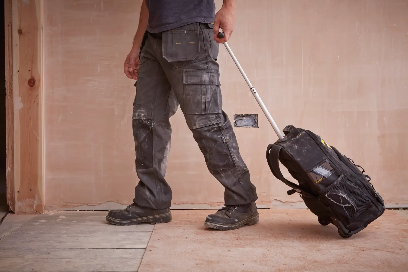 Mochila de ferramentas com rodas STANLEY STST83307-1 em obra, vista lateral, preta com detalhes amarelos.